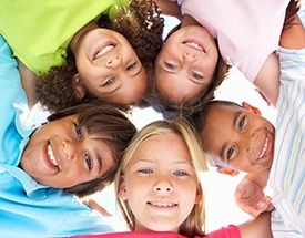 Group of kids with arms around each other looking down at camera