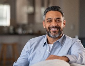 Man with dentures smiling while relaxing on couch