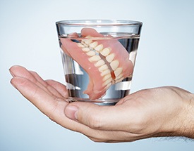 Hand holding full denture in glass of water