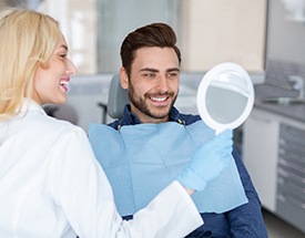 a dentist holding up a mirror for her patient to look at his smile
