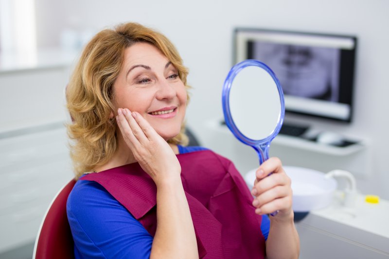 a woman looking at her smile in the mirror at the dentist’s office