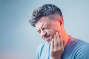 man in blue shirt with toothache who needs to see his dentist 