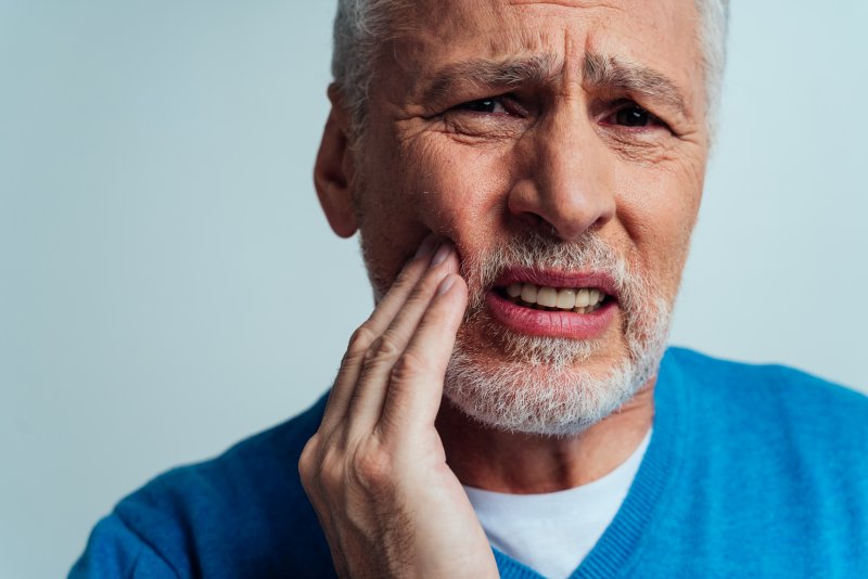 a man touching his cheek due to ill-fitting dentures